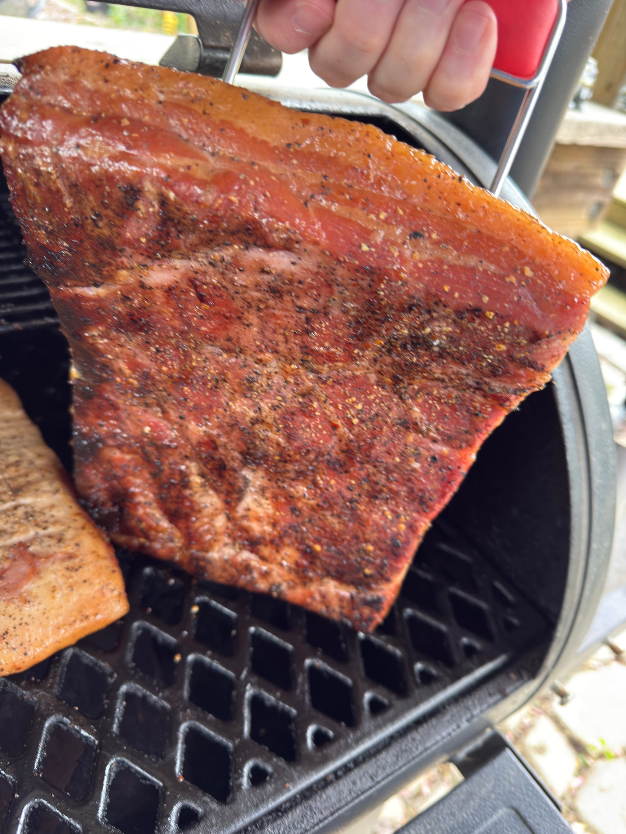 A chunk of pork belly being held up to show the crust it's developed from the pellet grill smoker.