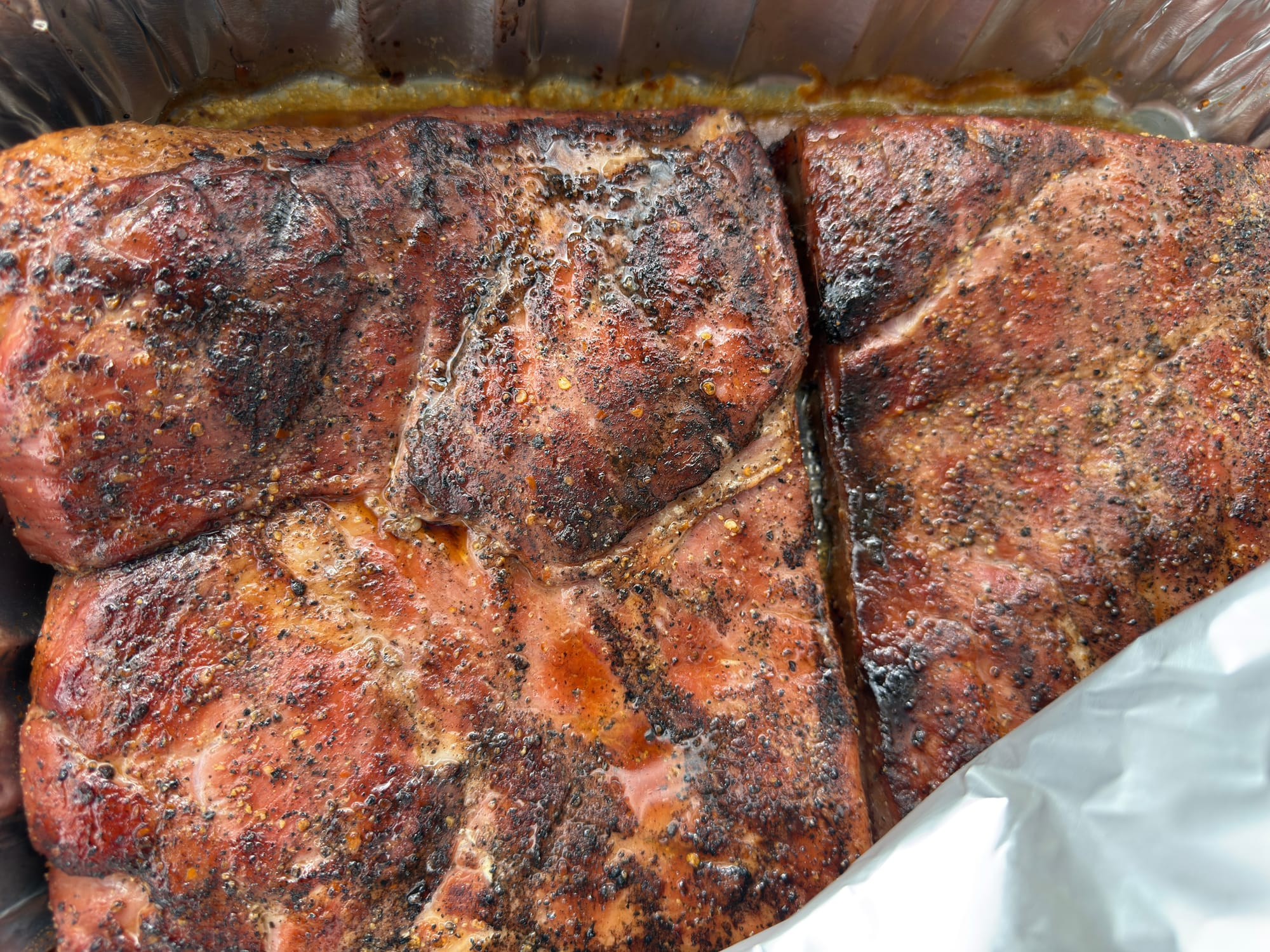 Pork belly cooking fat-side down in a foil pan.