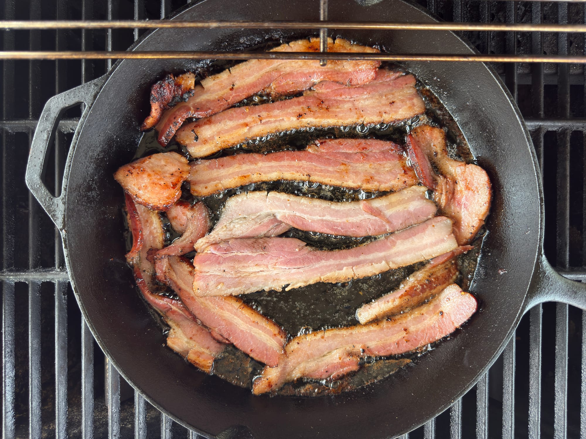More bacon slices in a cast iron skillet on the grill.