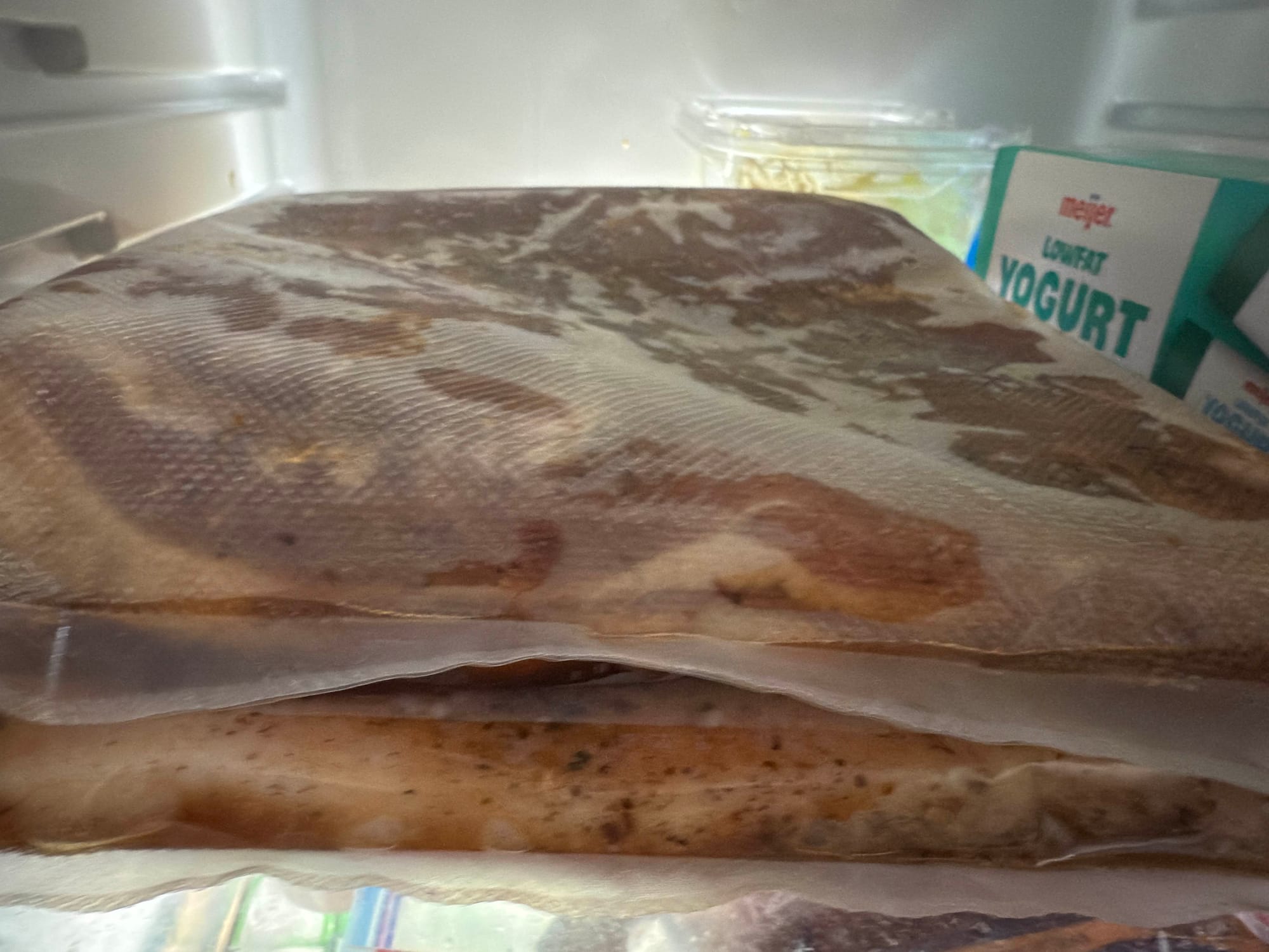 Two chunks of pork belly curing in vacuum-sealed bags in the fridge.