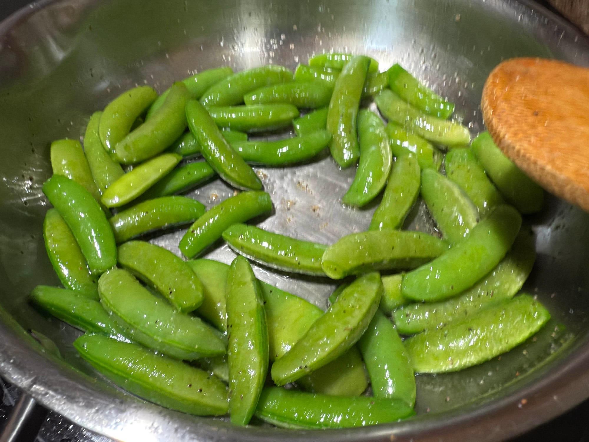 A stainless steel skillet full of seasoned sugar snap peas frying in oil.
