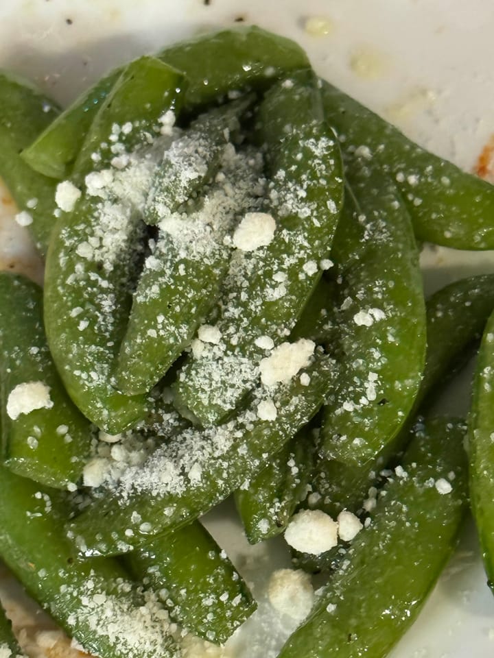 A plate of fried sugar snap peas with visible salt and parmesan on top.